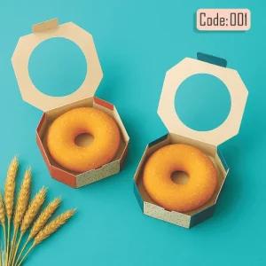 Two donuts in donut boxes hexagonal packaging, one plain and one with a golden hue, placed on a turquoise background with wheat stalks